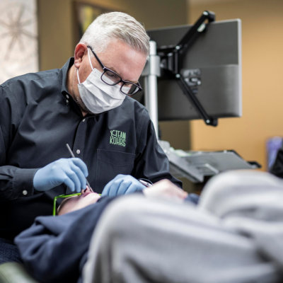 An orthodontist wearing a face mask and blue gloves carefully examines a patient with a bad bite in a clinical setting