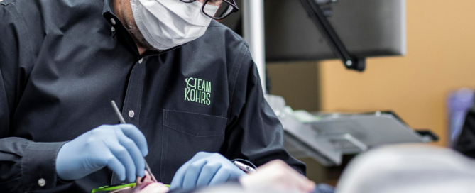 An orthodontist wearing a face mask and blue gloves carefully examines a patient with a bad bite in a clinical setting