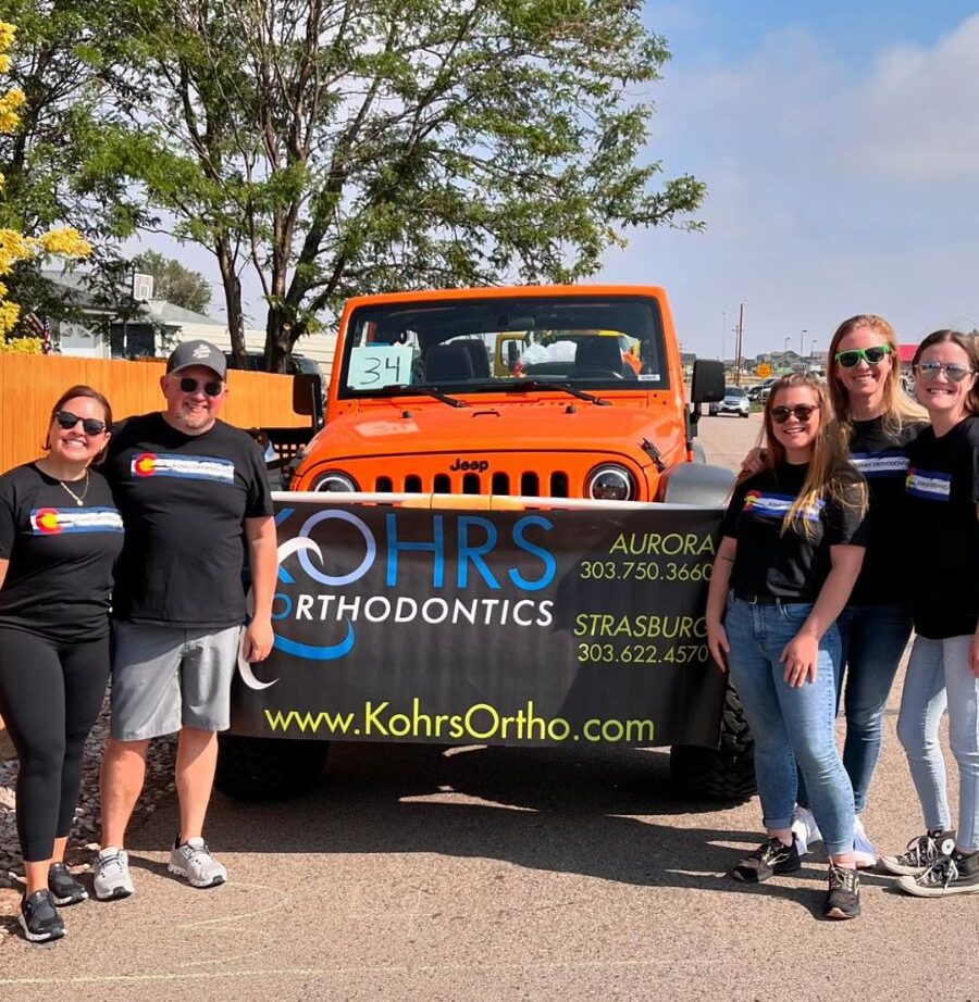 Top rated Kohrs Orthodontics team gathered in front of branded truck with banner in Meadow Hills