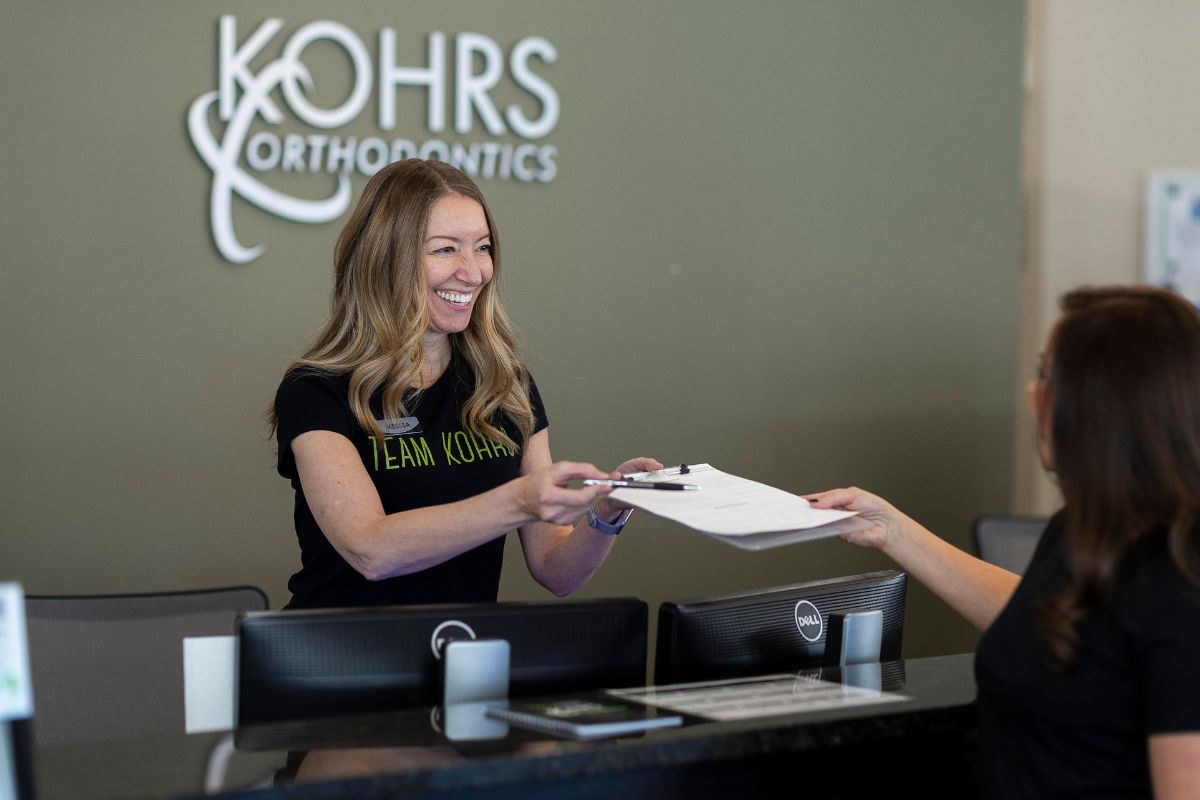Patient handing a clipboard to the front desk team at Kohrs Orthodontics Aurora West in Colorado, home to expert, top-rated orthodontic care